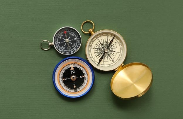Vier verschiedene Kompasse liegen auf einer grünen Unterlage, darunter ein goldener Kompass und zwei magnetische Modelle.