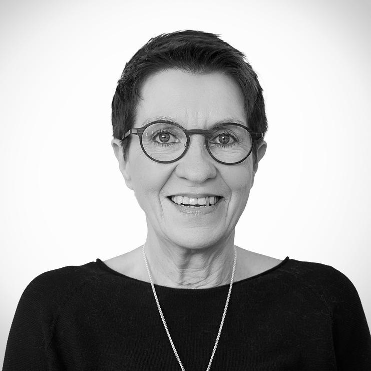 Portr&auml;t einer l&auml;chelnden Frau mit Kurzhaarschnitt, Brille und schwarzem Oberteil vor neutralem Hintergrund.